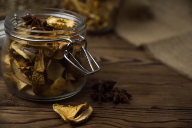 Ev yapımı kavrulmuş, kurutulmuş organik elma dilimleri. Kahverengi ahşap zemin üzerinde cam kavanozda baharat bulunan elma cipslerini metin için kopyalama alanı ile kapat