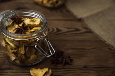 Ev yapımı kavrulmuş, kurutulmuş organik elma dilimleri. Kahverengi ahşap zemin üzerinde cam kavanozda baharat bulunan elma cipslerini metin için kopyalama alanı ile kapat