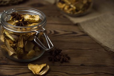 Ev yapımı kavrulmuş, kurutulmuş organik elma dilimleri. Kahverengi ahşap zemin üzerinde cam kavanozda baharat bulunan elma cipslerini metin için kopyalama alanı ile kapat