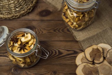 Ev yapımı kavrulmuş, kurutulmuş organik elma dilimleri. Kahverengi ahşap zemin üzerinde cam kavanozda baharat bulunan elma cipslerini metin için kopyalama alanı ile kapat