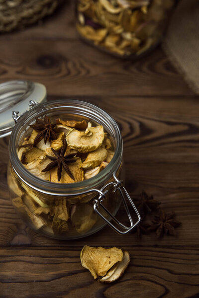 Homemade crispy sun dried organic apple slices. Close up of apple chips with spice in glass jar on brown wooden background with copy space for text