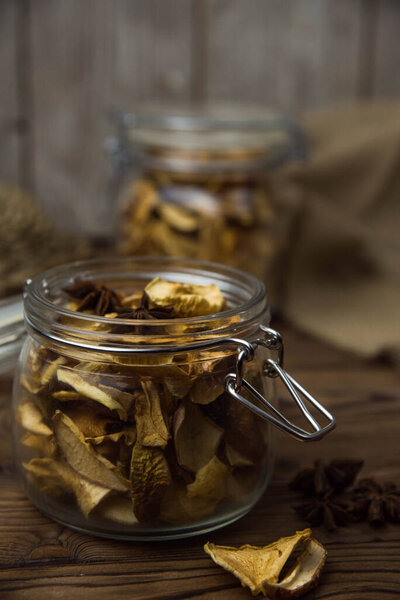 Homemade crispy sun dried organic apple slices. Close up of apple chips with spice in glass jar on brown wooden background with copy space for text