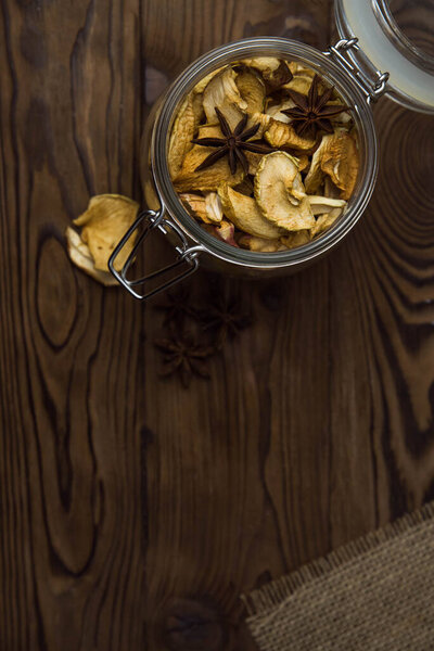 Homemade crispy sun dried organic apple slices. Close up of apple chips with spice in glass jar on brown wooden background with copy space for text