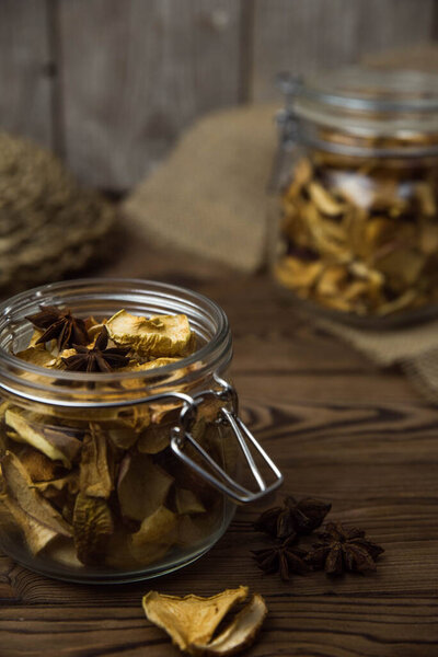 Homemade crispy sun dried organic apple slices. Close up of apple chips with spice in glass jar on brown wooden background with copy space for text
