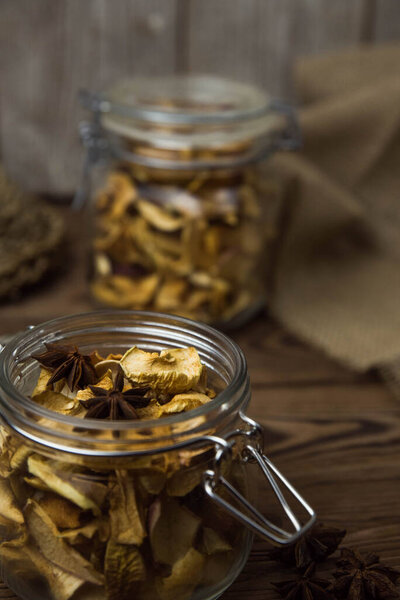 Homemade crispy sun dried organic apple slices. Close up of apple chips with spice in glass jar on brown wooden background with copy space for text