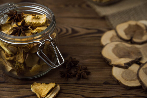 Homemade crispy sun dried organic apple slices. Close up of apple chips with spice in glass jar on brown wooden background with copy space for text
