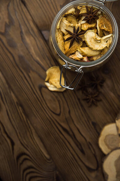 Homemade crispy sun dried organic apple slices. Close up of apple chips with spice in glass jar on brown wooden background with copy space for text
