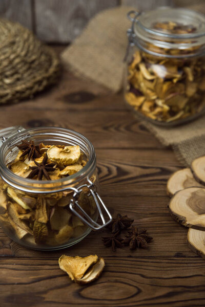 Homemade crispy sun dried organic apple slices. Close up of apple chips with spice in glass jar on brown wooden background with copy space for text