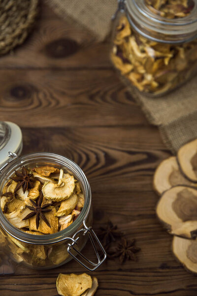 Homemade crispy sun dried organic apple slices. Close up of apple chips with spice in glass jar on brown wooden background with copy space for text