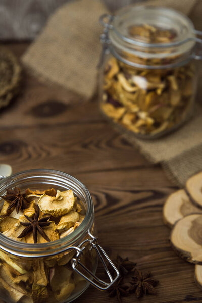 Homemade crispy sun dried organic apple slices. Close up of apple chips with spice in glass jar on brown wooden background with copy space for text