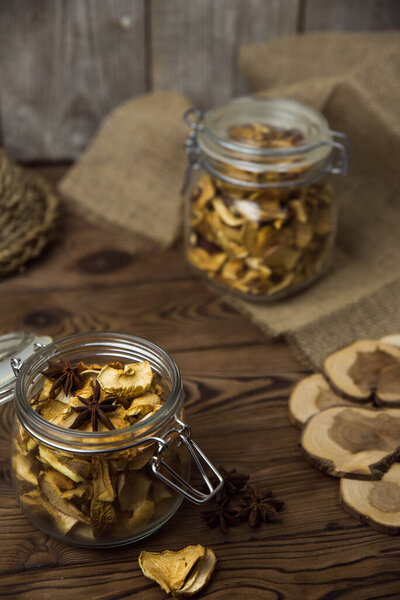 Homemade crispy sun dried organic apple slices. Close up of apple chips with spice in glass jar on brown wooden background with copy space for text