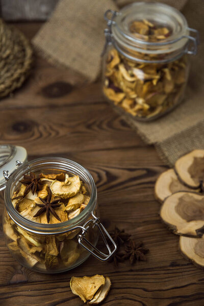 Homemade crispy sun dried organic apple slices. Close up of apple chips with spice in glass jar on brown wooden background with copy space for text