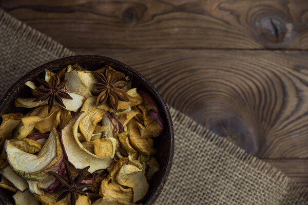 Homemade crispy sun dried organic apple slices. Close up of apple chips with spice in bowl on brown wooden background with copy space for text