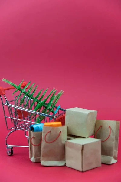 Happy New Year and Merry Christmas concept. Shopping cart with purchases and Christmas tree  - packages and boxes on red  background with copy space isolated. Online shopping and holiday sale concept.