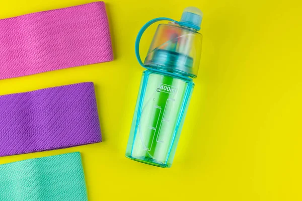 Colorful fitness gums on pink background. Elastic expanders and tapes of different color. Colored rubber and textile bands, bottle of water and massage myofascial ball. Home fitness equipment.