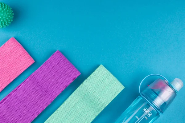 Pembe arka planda renkli fitness dişetleri. Elastik genişleticiler ve farklı renkte kasetler. Renkli lastik ve tekstil bantları, bir şişe su ve masaj miyofasyal topu. Evde spor aletleri.