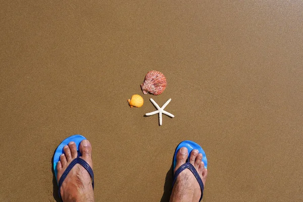 ビーチの砂の上に青いフリップフロップサンダル ヒトデや貝殻を持つ男の足 夏休みのコンセプト — ストック写真