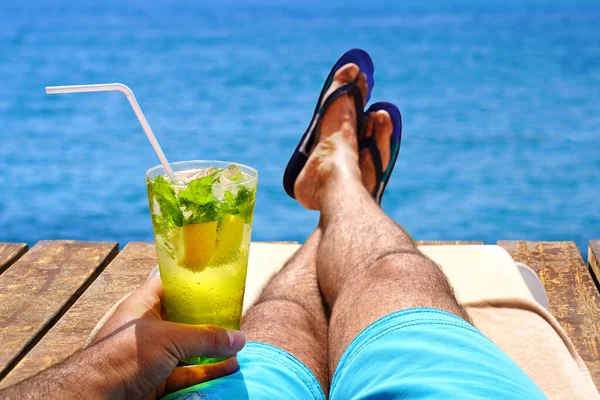 木のビーチ桟橋で冷たいモヒートドリンクで日向ぼっこや日光浴をする男 夏休みのコンセプトイメージ ストック写真