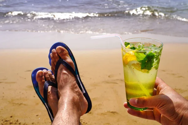 砂浜で冷たいモヒートを飲みながら 日向ぼっこや日光浴をする男 夏休みのコンセプトイメージ ストック画像