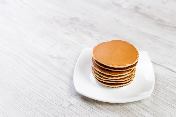 Leckere Pfannkuchen auf weißem Teller, Holzboden, Ahornsirup — Stockfoto