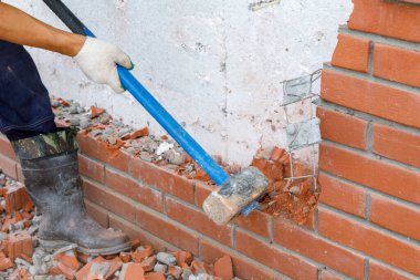 İnşaatçı bir araçla duvarın tuğla işçiliğini kırar.