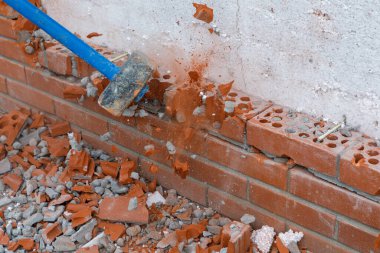 İnşaatçı bir araçla duvarın tuğla işçiliğini kırar.