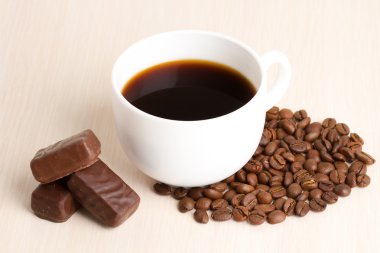 Kahve fincanı ve kahve çekirdekleri ahşap masada.