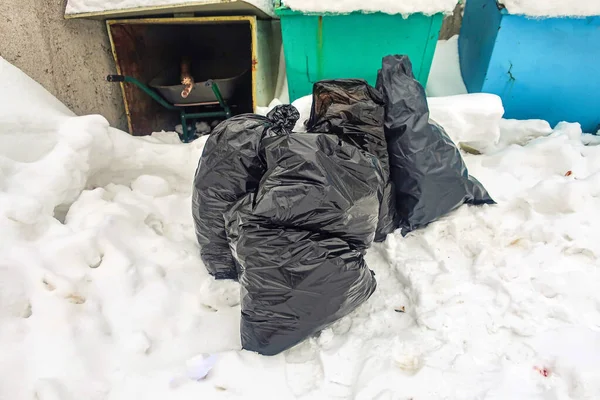 garbage packed in black plastic bags in the snow by the dumpsters