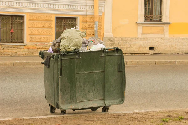 overflowing green trash can on wheels on the road