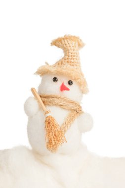 Beyaz arka planda süpürgeyle kar süpüren şapkalı ve fularlı oyuncak kardan adam.