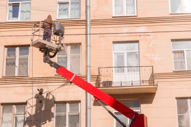 Kaldıraç platformunda çalışan bir işçi evin ön cephesini hortumla yıkıyor.