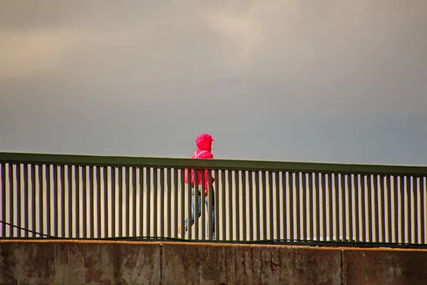 Man Pink Jacket Walks Bridge Rain Covered Sky — Zdjęcie stockowe
