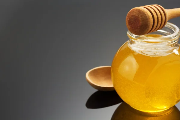 Glass jar of honey and stick on black — Stock Photo, Image
