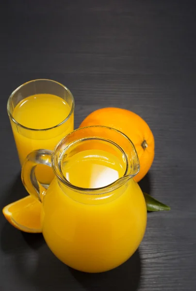Jarro de vidro e suco de laranja na madeira — Fotografia de Stock