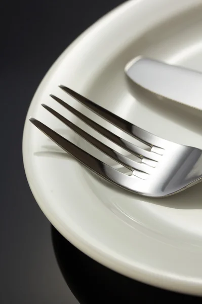 Knife and fork at plate on black — Stock Photo, Image