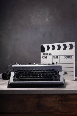 vintage typewriter, camera and movie clapper board at wooden table near wall background surface, abstract retro writer concept