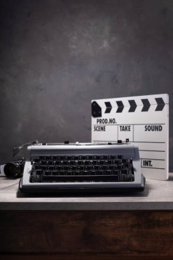 vintage typewriter, camera and movie clapper board at wooden table near wall background surface, abstract retro writer concept clipart