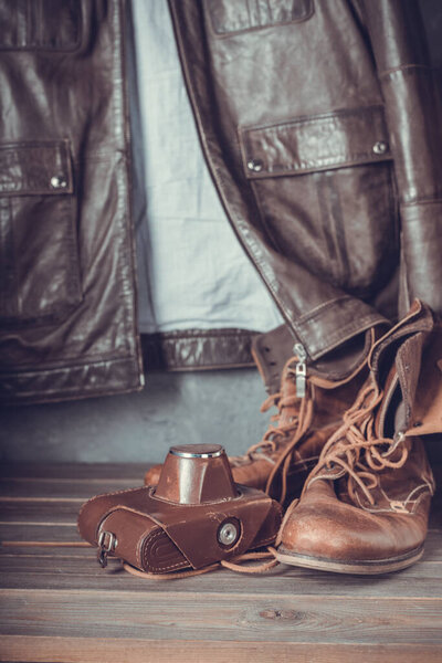 travel vintage old boots shoes at wooden table and jacket, concrete wall background texture surface