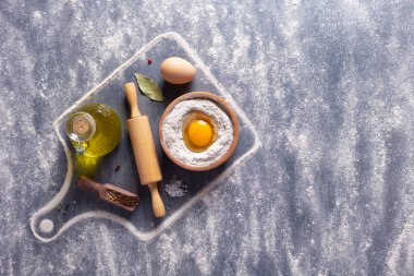 Masada ev yapımı ekmek pişirmek için un tozu ve fırın malzemeleri var. Hamur tarifi için yumurtalı buğday unu yiyeceği. Taş arka plan dokusunda fotokopi alanı ve düz konsept ile üst görünüm.