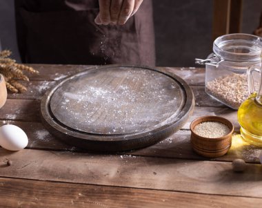 Fırıncı, hamur yoğurmak ve ahşap masada ev yapımı ekmek pişirmek için un saçıyor. Erkek eli ve ahşap pizza tahtası masa arkası desenli fırın konsepti