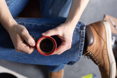 Kot pantolonun içinde bir fincan kahve ve bir bacak tutan erkeklerin elleri ve eski deri çizmeler. Rahatla ve sanat müziği yaşam tarzı konsepti