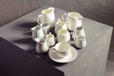 Boş süt kavanozları ya da krema kapları seti. Mutfak bulaşık takımı ve sofra takımı duvar arkası dokusu yakınındaki gri küpte.