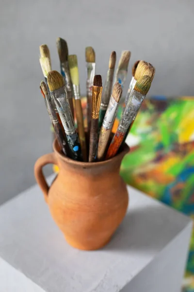 Paint brush in clay jug and palette on wooden table background. Oil painting  and art still life Stock Photo by seregam