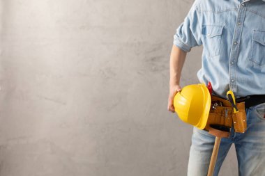 Duvarın yanında miğfer ve alet kemeri tutan bir işçi. Erkek eli ve inşaat aletleri. Yenileme veya onarım konsepti