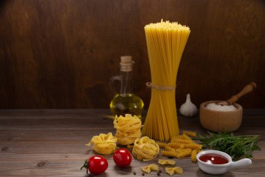 Ahşap masa arkasında makarna ve yiyecek malzemesi. Masada çiğ İtalyan yemeği çeşitleri var.