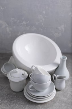 Boş çanak çömlek seti ya da beyaz seramik tabaklar. Beyaz mutfak bulaşık takımı ve sofra takımı gri duvar arkaplan dokusunun yanındaki masada.