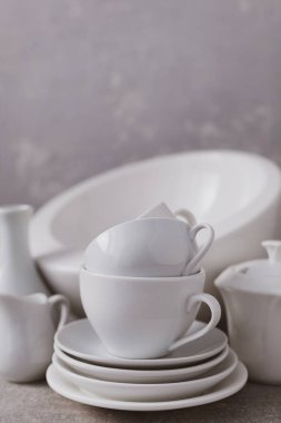 Boş çanak çömlek seti ya da beyaz seramik tabaklar. Beyaz mutfak bulaşık takımı ve sofra takımı gri duvar arkaplan dokusunun yanındaki masada.