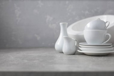 Boş çanak çömlek seti ya da seramik tabak. Beyaz mutfak bulaşık takımı ve sofra takımı gri duvar arkaplan dokusunun yanındaki masada.
