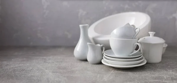 Empty crockery set or white ceramic dishes. White kitchen dishware and tableware on table near grey wall background texture