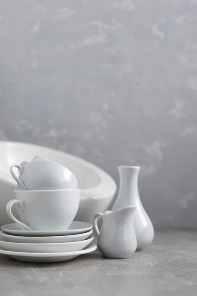 Empty crockery set or ceramic dishes. White kitchen dishware and tableware on table near grey wall background texture